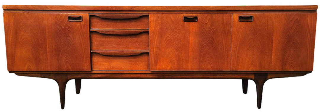 Luxuriously Long cocktail credenza designed and manufactured by Greaves & Thomas.  Beautifully figured Southeast Asian crown-cut teak wood with African afrormosia wood inset and curved pulls, tapered legs, and curved apron.  The flat top surmounts a case offering storage cabinets with shelves on each end; three storage drawers at center left; and a flap-front cocktail cabinet at center right.  The top drawer is divided for cutlery organization.  The cocktail cabinet features a drawer fitted with sections for cocktail prep storage.
