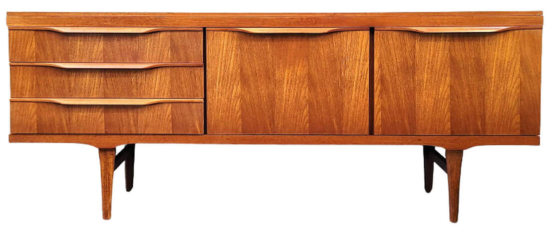 Elliott's of Newbury vintage teak credenza is on tapered legs with side stretchers.  The carcase is fitted with three drawers on the left. To the right of the drawers is a rare double cocktail cabinet with two fall-front doors.