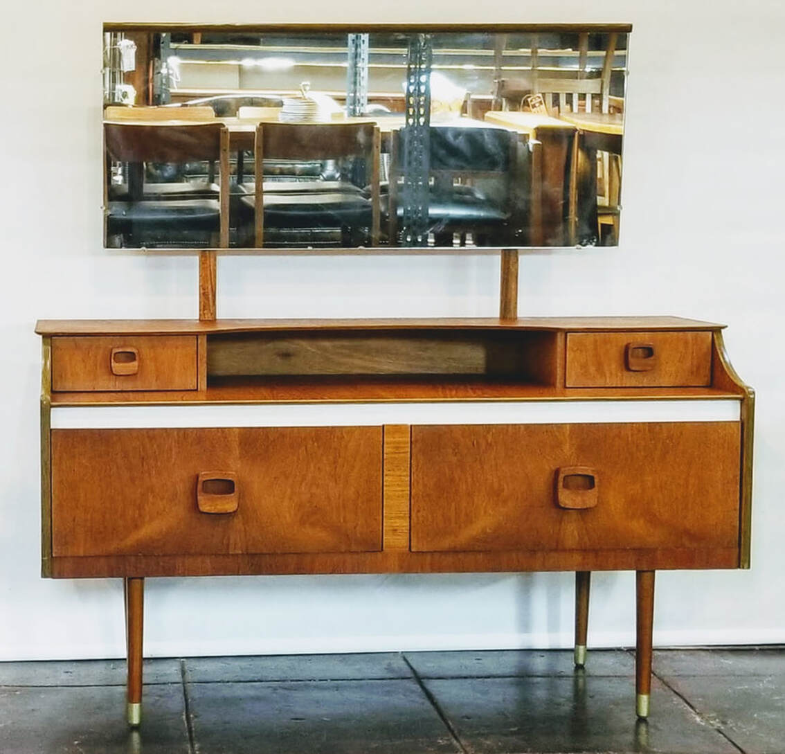 Mid-Century Modern mirrored bedroom vanity from England has four storage drawers with stylized wooden pulls. The straight cylinder legs end in brass caps.